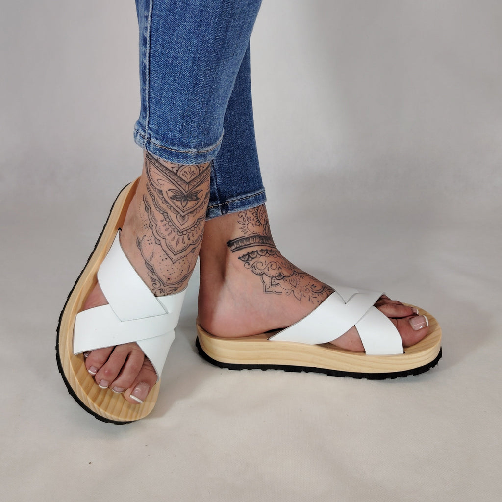 Sandalia plana de madera natural con tiras cruzadas de color blanco y diseño artesanal de verano.