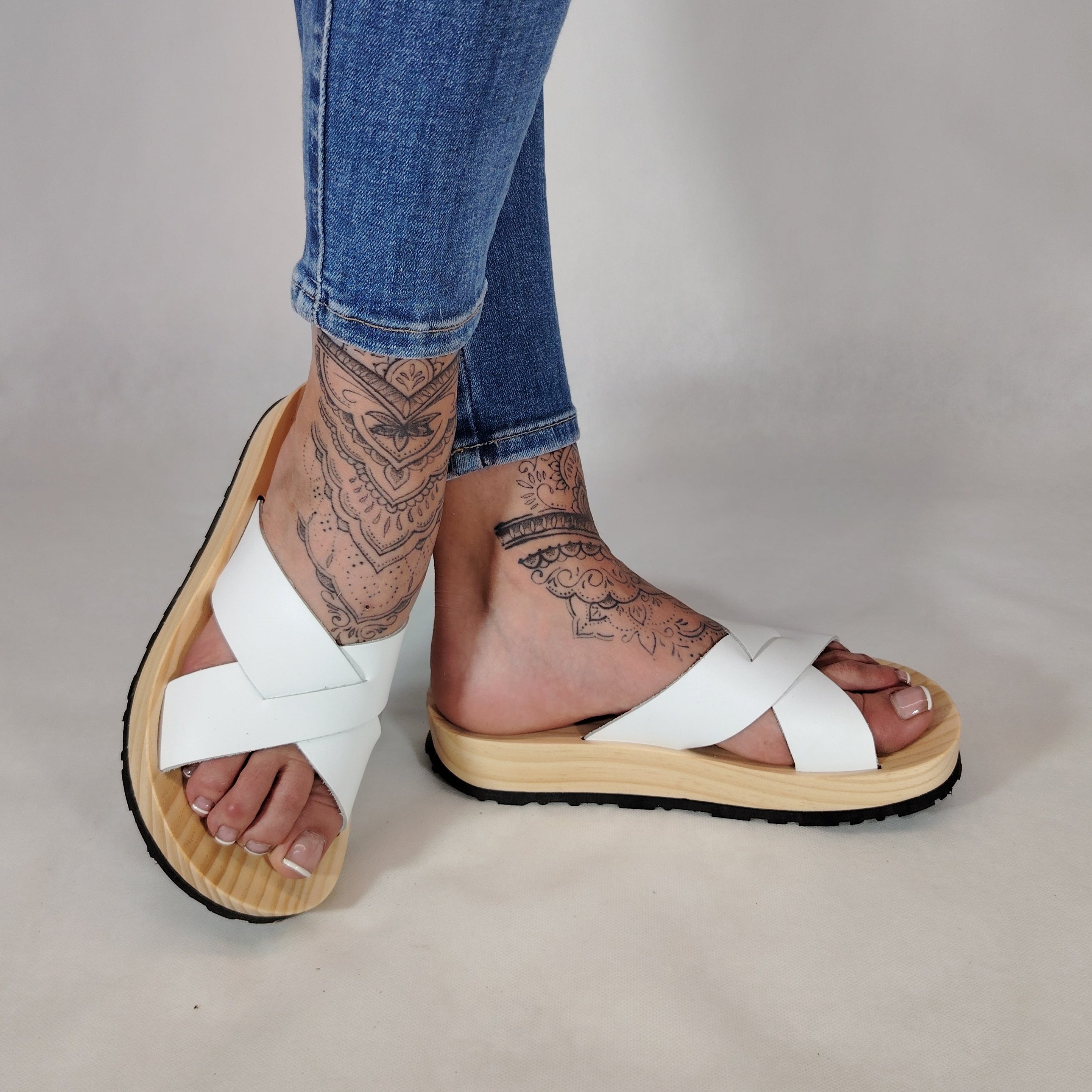 Sandalia plana de madera natural con tiras cruzadas de color blanco y diseño artesanal de verano.