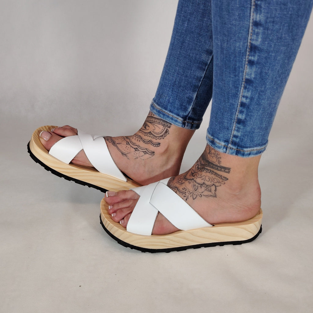 Sandalia plana de madera natural con tiras cruzadas de color blanco y diseño artesanal de verano.