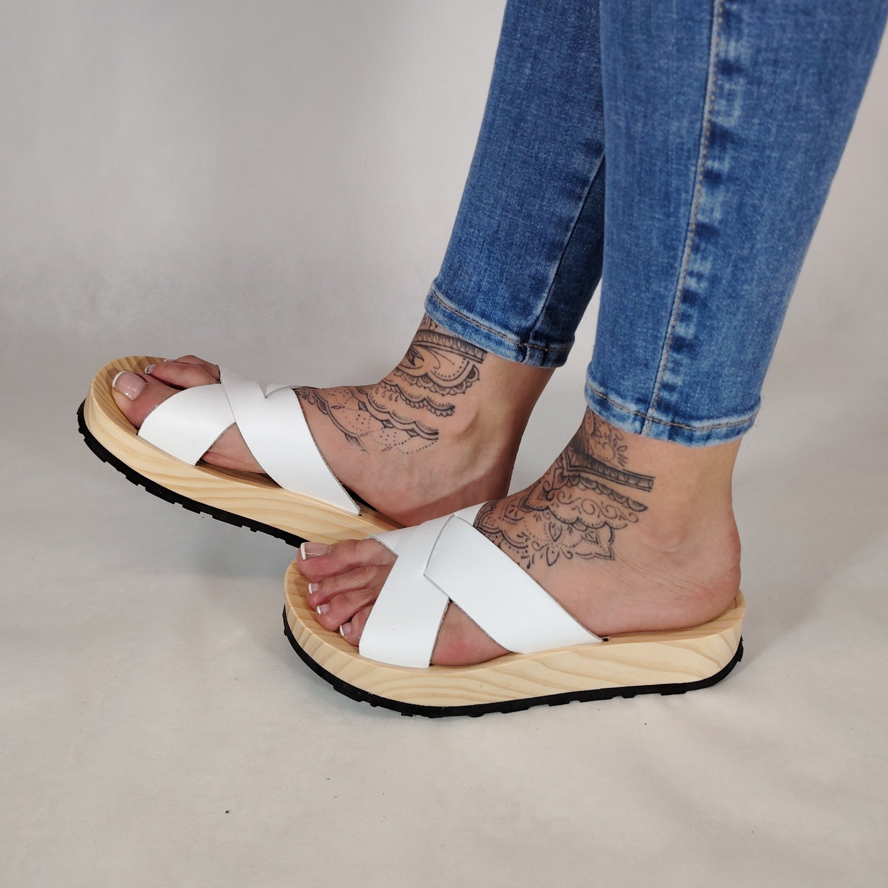 Sandalia plana de madera natural con tiras cruzadas de color blanco y diseño artesanal de verano.
