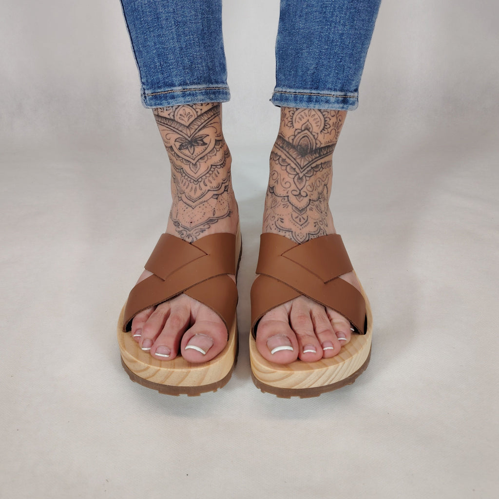 Sandalia plana de madera natural con tiras cruzadas de color cuero y diseño artesanal de verano.