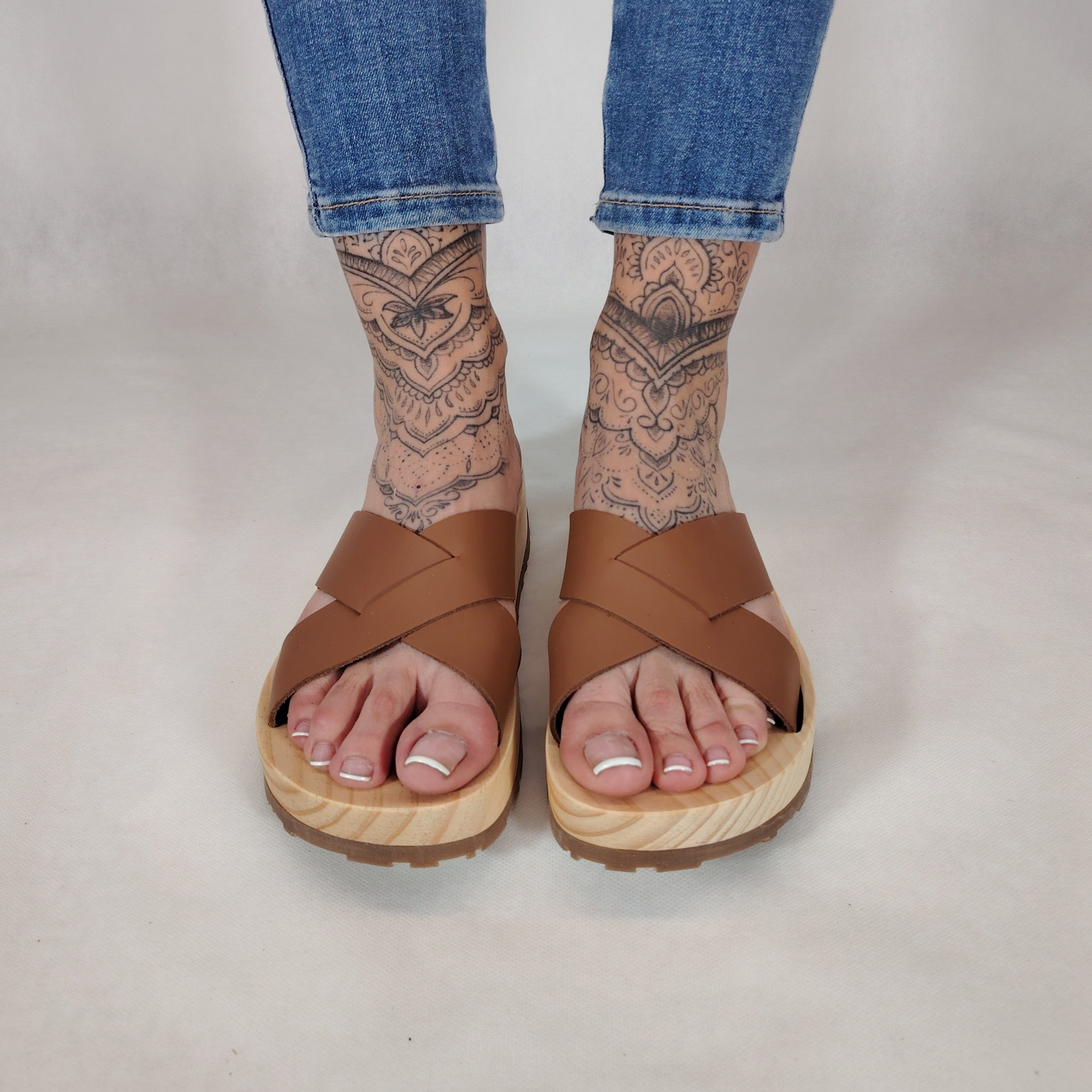 Sandalia plana de madera natural con tiras cruzadas de color cuero y diseño artesanal de verano.