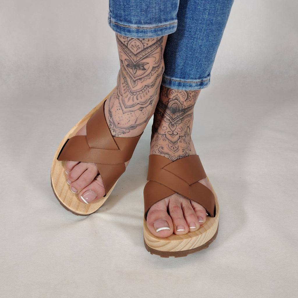 Sandalia plana de madera natural con tiras cruzadas de color cuero y diseño artesanal de verano.