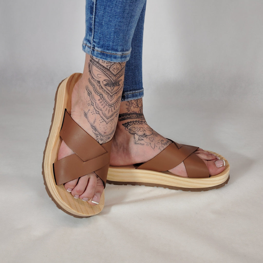 Sandalia plana de madera natural con tiras cruzadas de color cuero y diseño artesanal de verano.