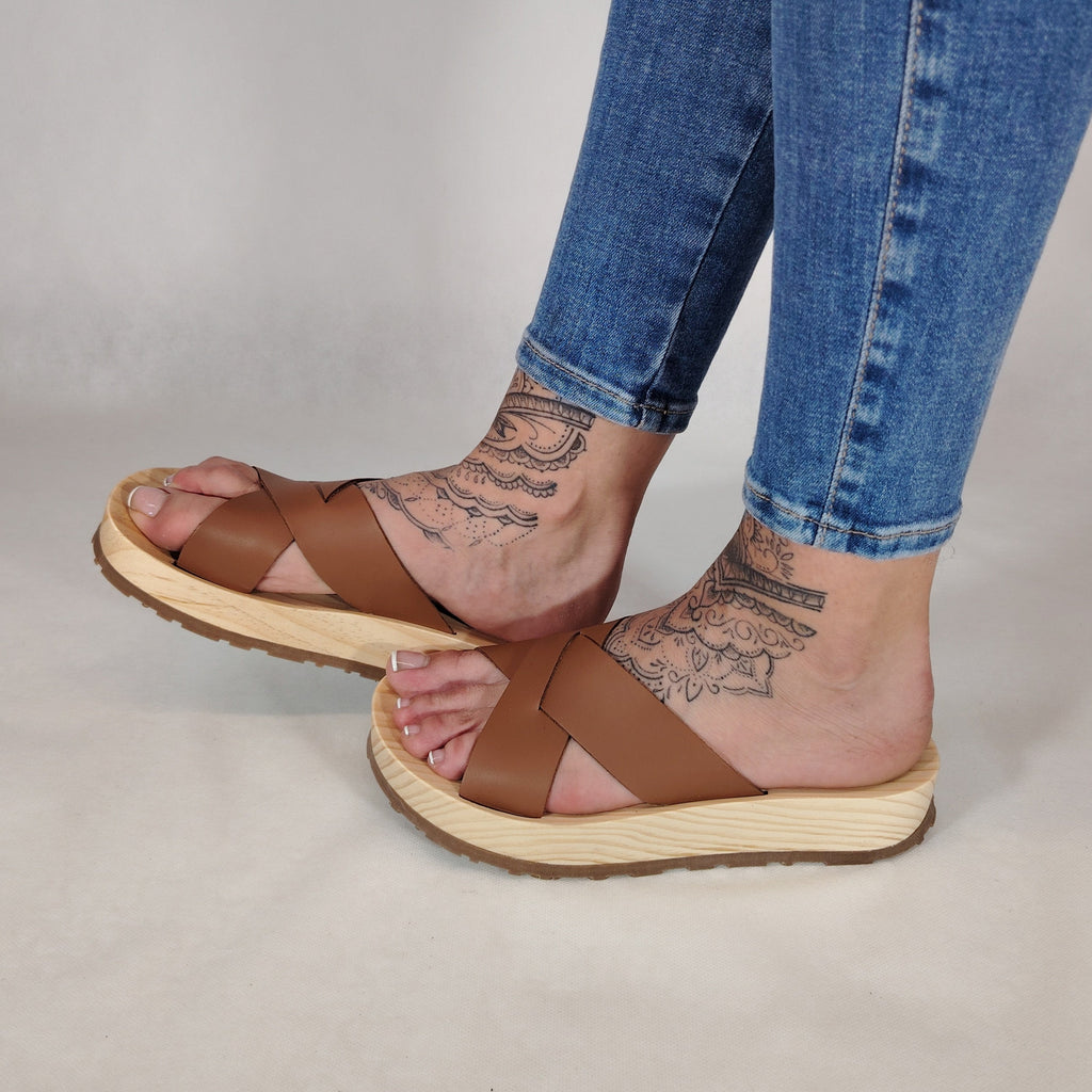 Sandalia plana de madera natural con tiras cruzadas de color cuero y diseño artesanal de verano.