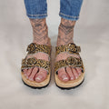 Sandalias tipo zueco de la marca Artichoke con base de madera, dos correas ajustables de cuero y piel sintética de estampado animal print leopard , y hebillas redondas de metal dorado.
