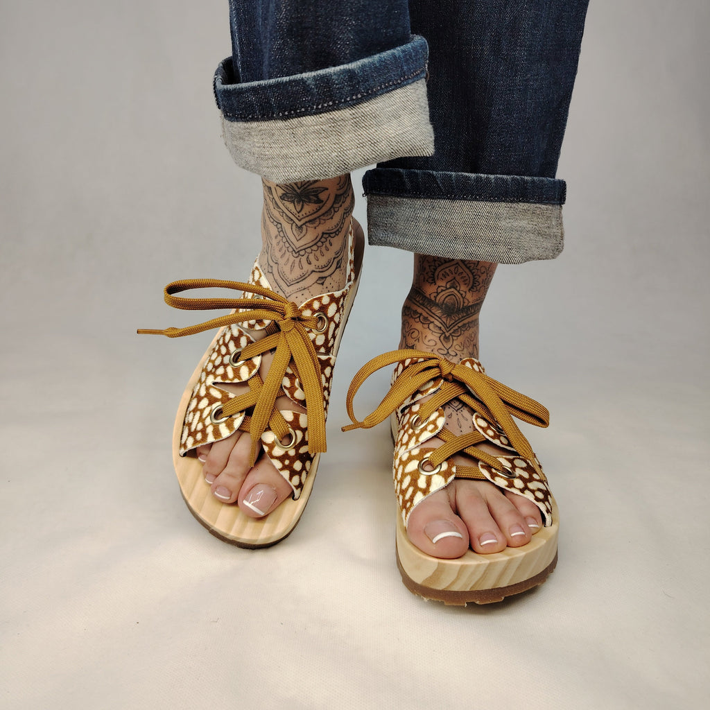 Sandalias de plataforma de madera natural artesanal con tira trasera y pala de piel efecto pelo con estampado de cervatillo y cordones marrones.