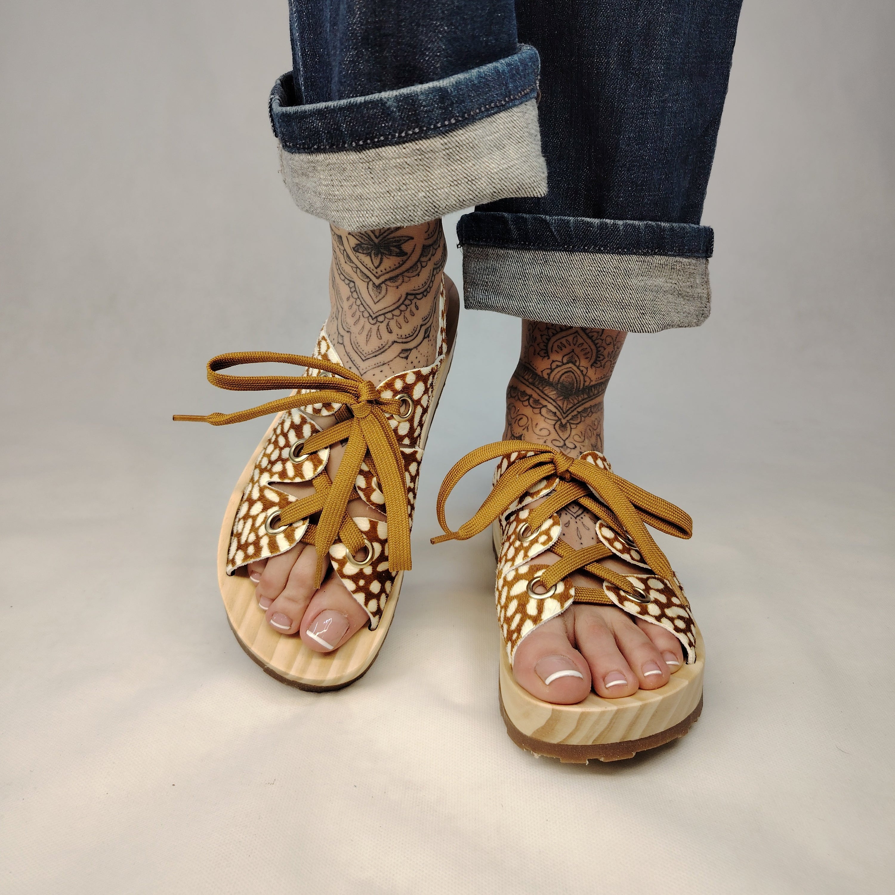 Sandalias de plataforma de madera natural artesanal con tira trasera y pala de piel efecto pelo con estampado de cervatillo y cordones marrones.