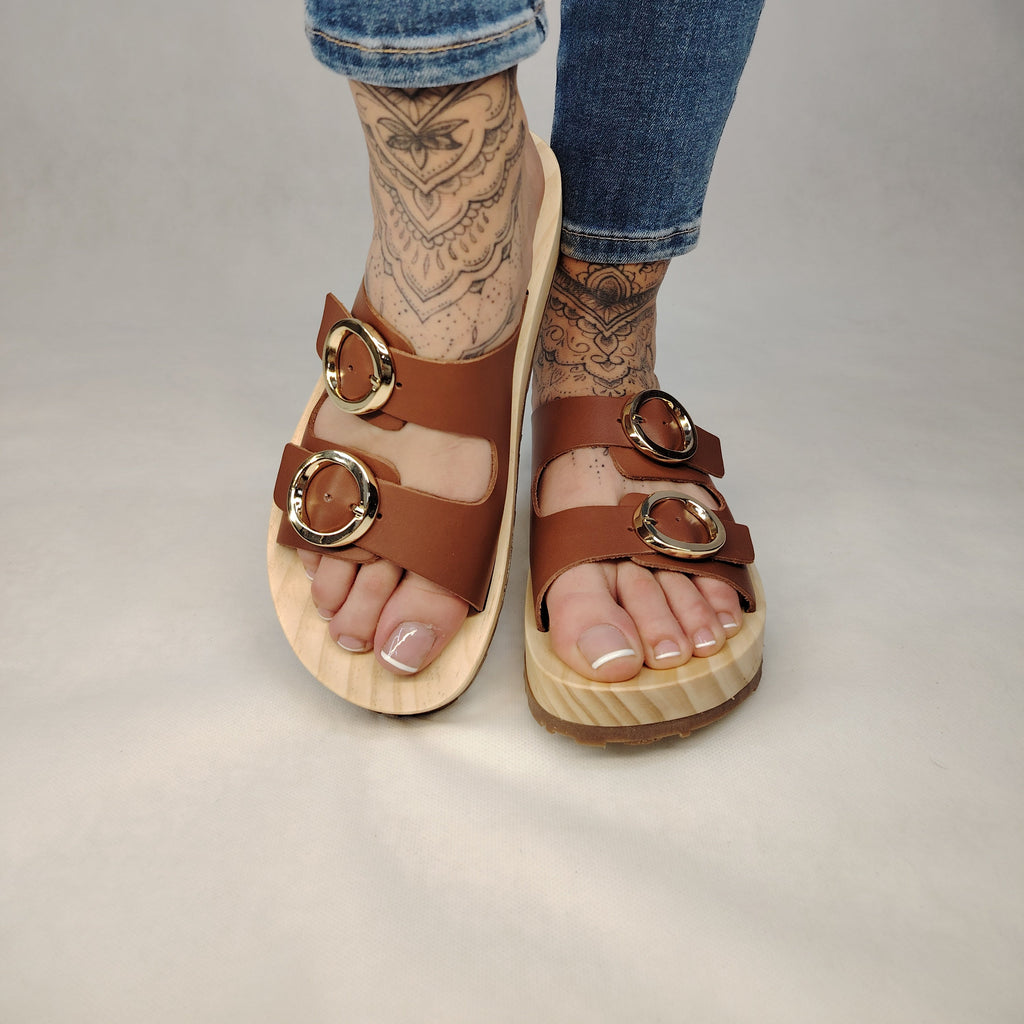 Sandalias tipo zueco de la marca Artichoke con base de madera, dos correas ajustables de cuero y piel sintética de estampado Marrón, y hebillas redondas de metal dorado.