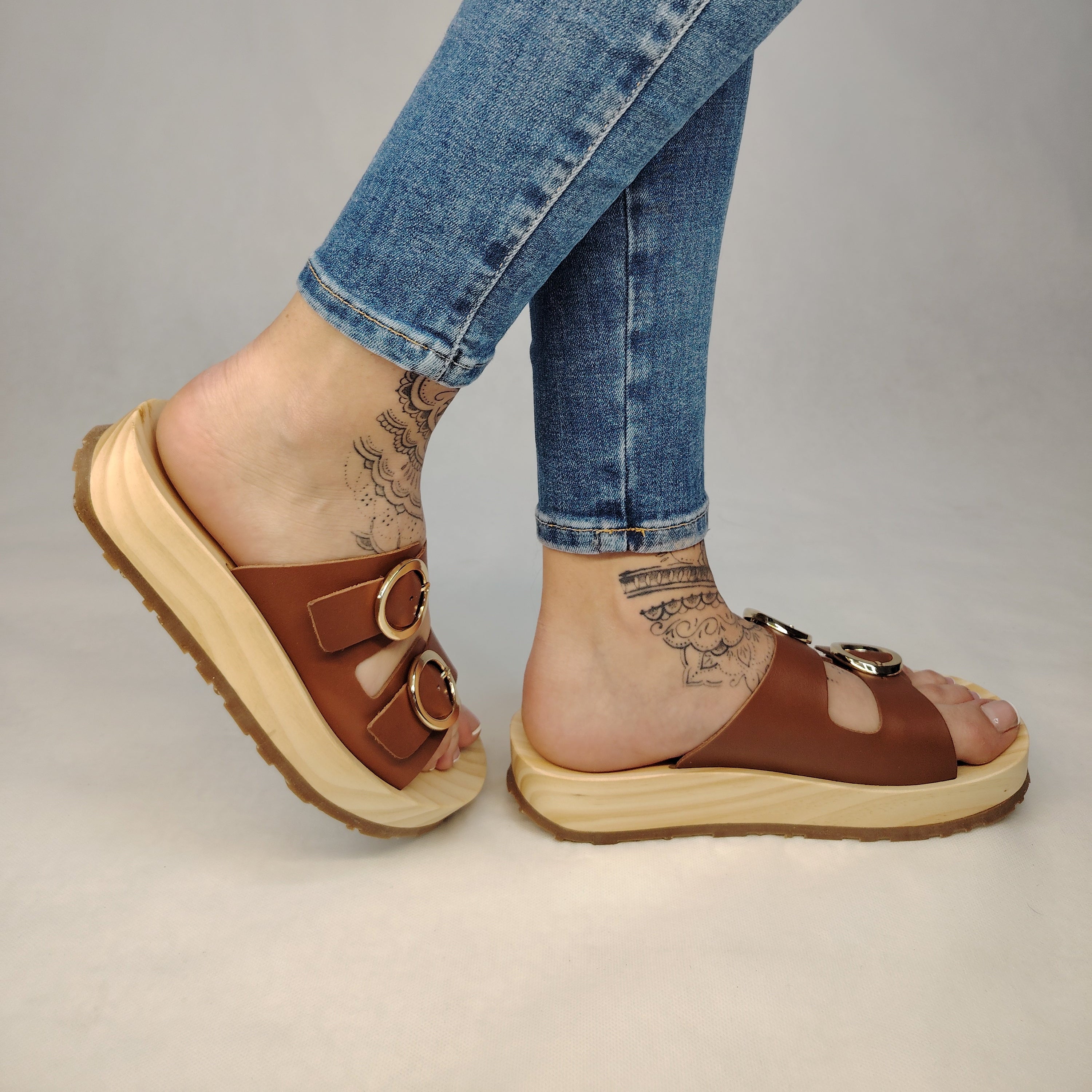 Sandalias tipo zueco de la marca Artichoke con base de madera, dos correas ajustables de cuero y piel sintética de estampado Marrón, y hebillas redondas de metal dorado.