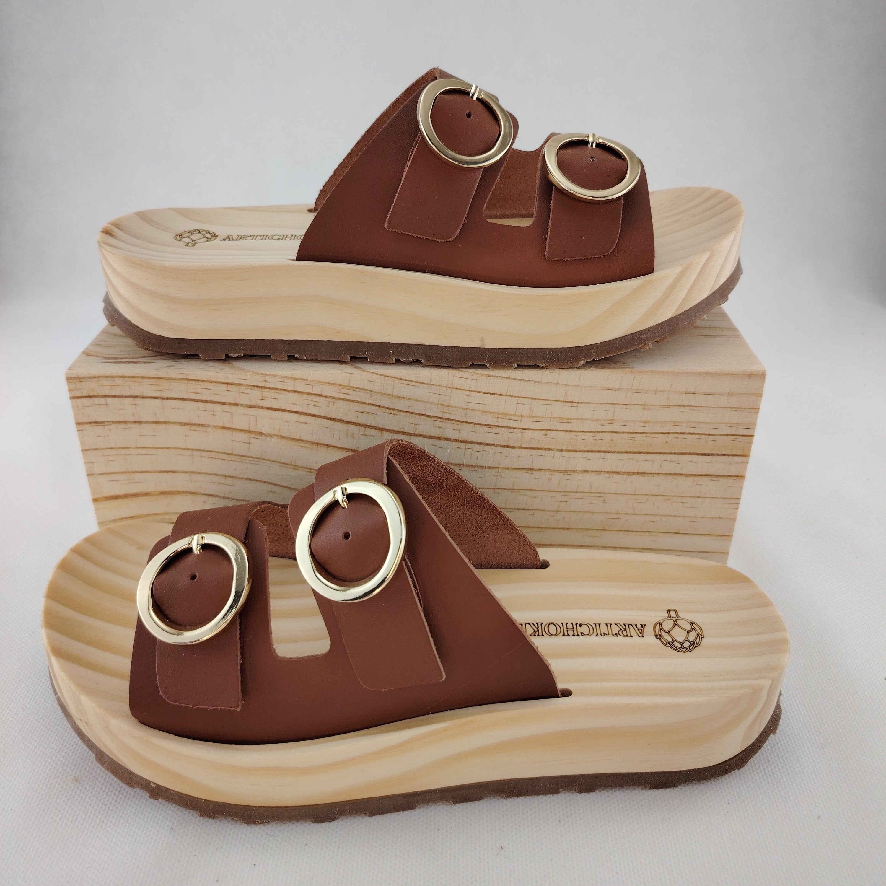 Sandalias tipo zueco de la marca Artichoke con base de madera, dos correas ajustables de cuero y piel sintética de estampado Marrón, y hebillas redondas de metal dorado.