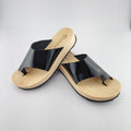 Sandalias planas de madera natural artesanal con pala de piel negra brillante y sujeción de dedo, calzado de verano minimalista sobre fondo blanco.