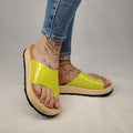 Sandalias planas de madera natural artesanal con pala de piel pistacho brillante y sujeción de dedo, calzado de verano minimalista sobre fondo blanco.