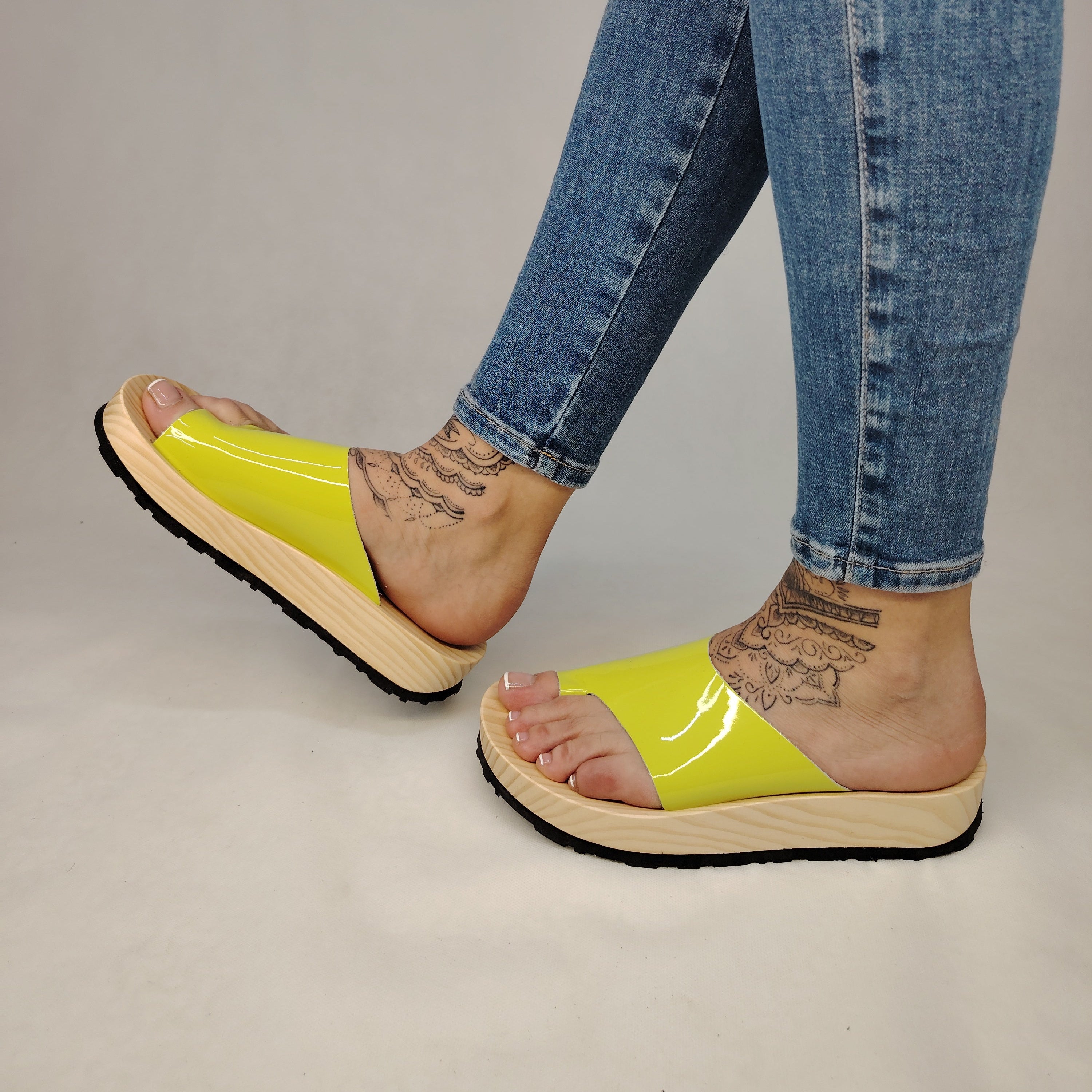 Sandalias planas de madera natural artesanal con pala de piel pistacho brillante y sujeción de dedo, calzado de verano minimalista sobre fondo blanco.