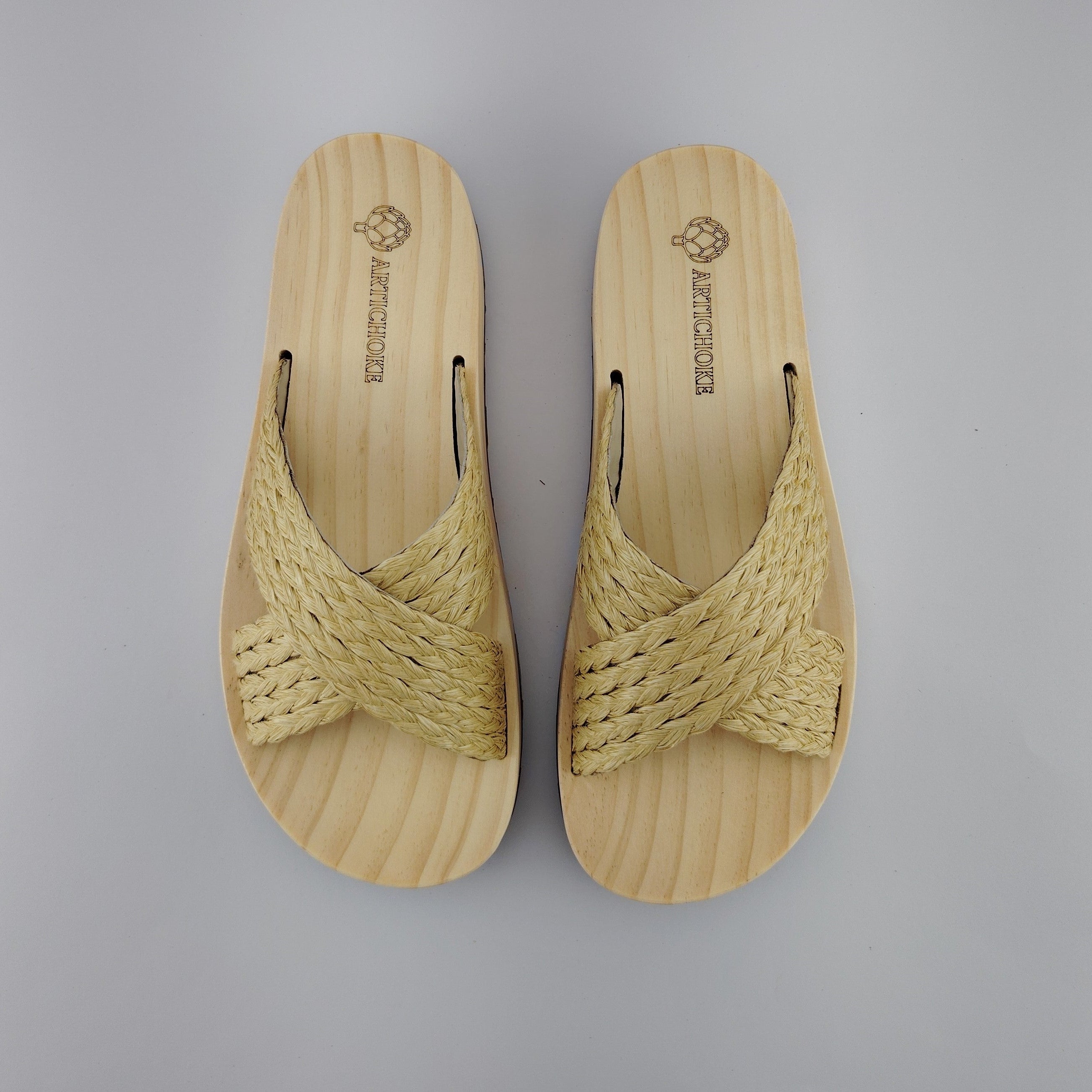 Sandalia plana de madera natural con tiras cruzadas de rafia trenzada en color natural y diseño artesanal de verano.