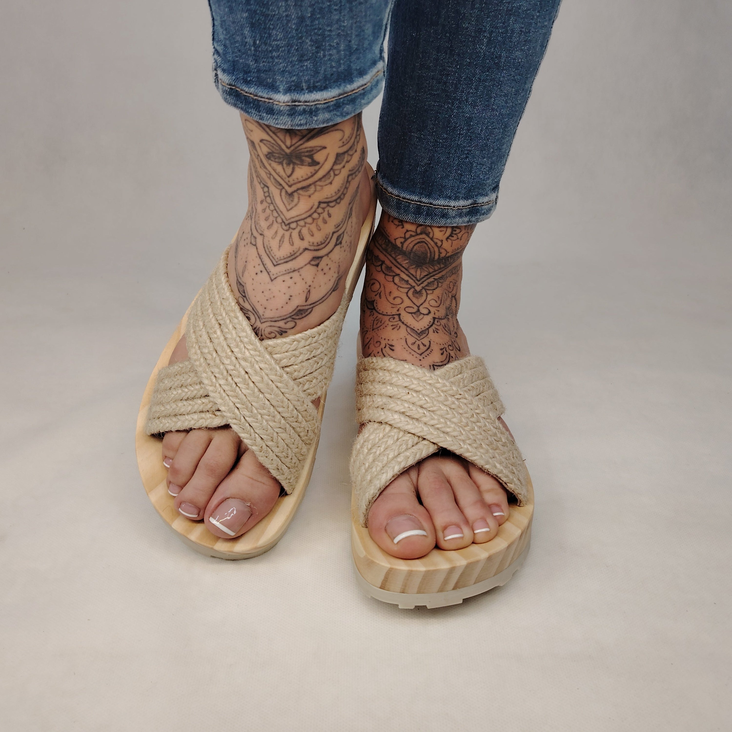 Sandalia plana de madera natural con tiras cruzadas de yute trenzada en color natural y diseño artesanal de verano.