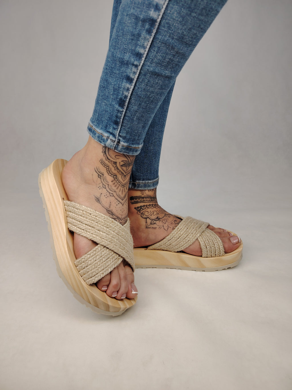 Sandalia plana de madera natural con tiras cruzadas de yute trenzada en color natural y diseño artesanal de verano.