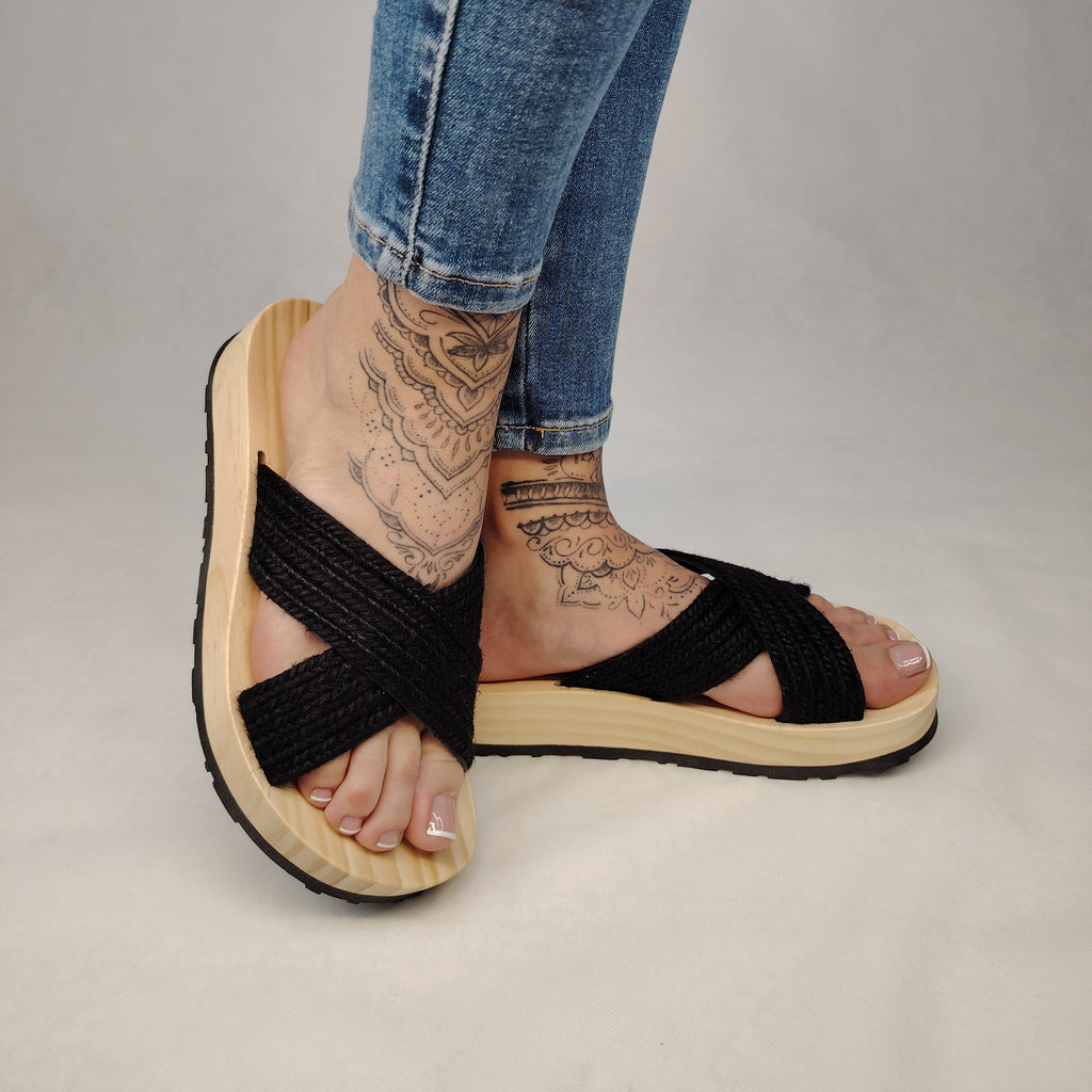Sandalia plana de madera natural con tiras cruzadas de yute trenzada en color negro y diseño artesanal de verano.