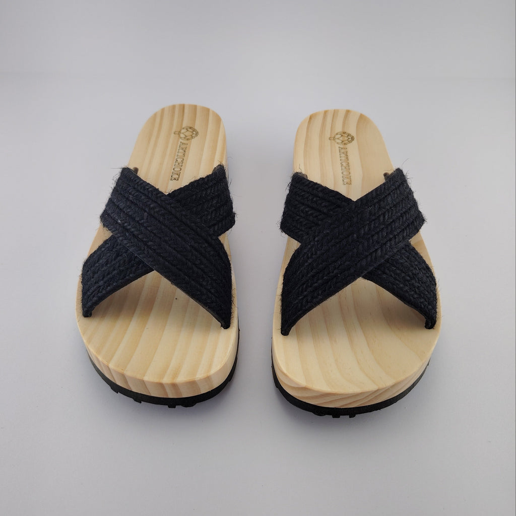 Sandalia plana de madera natural con tiras cruzadas de yute trenzada en color negro y diseño artesanal de verano.