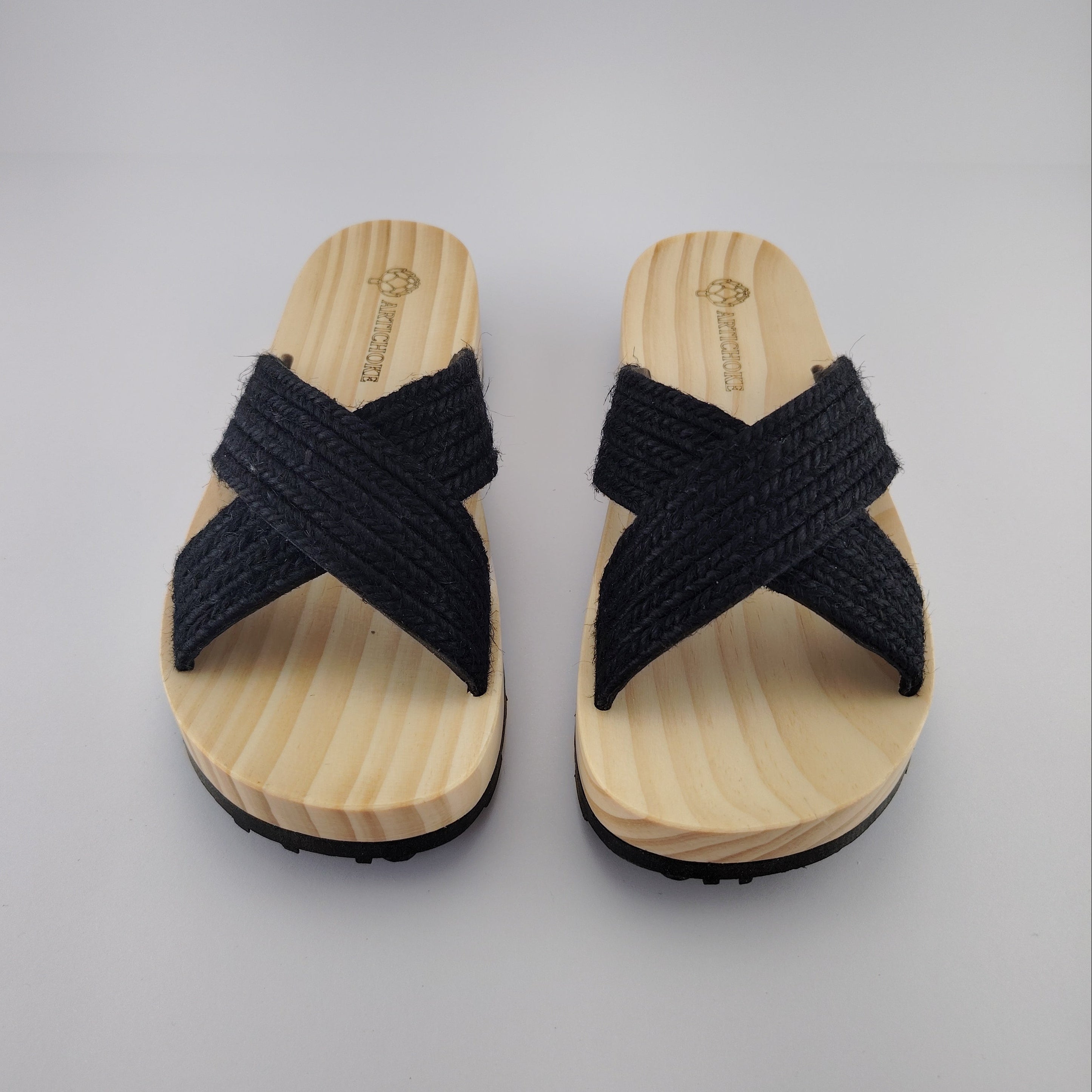 Sandalia plana de madera natural con tiras cruzadas de yute trenzada en color negro y diseño artesanal de verano.