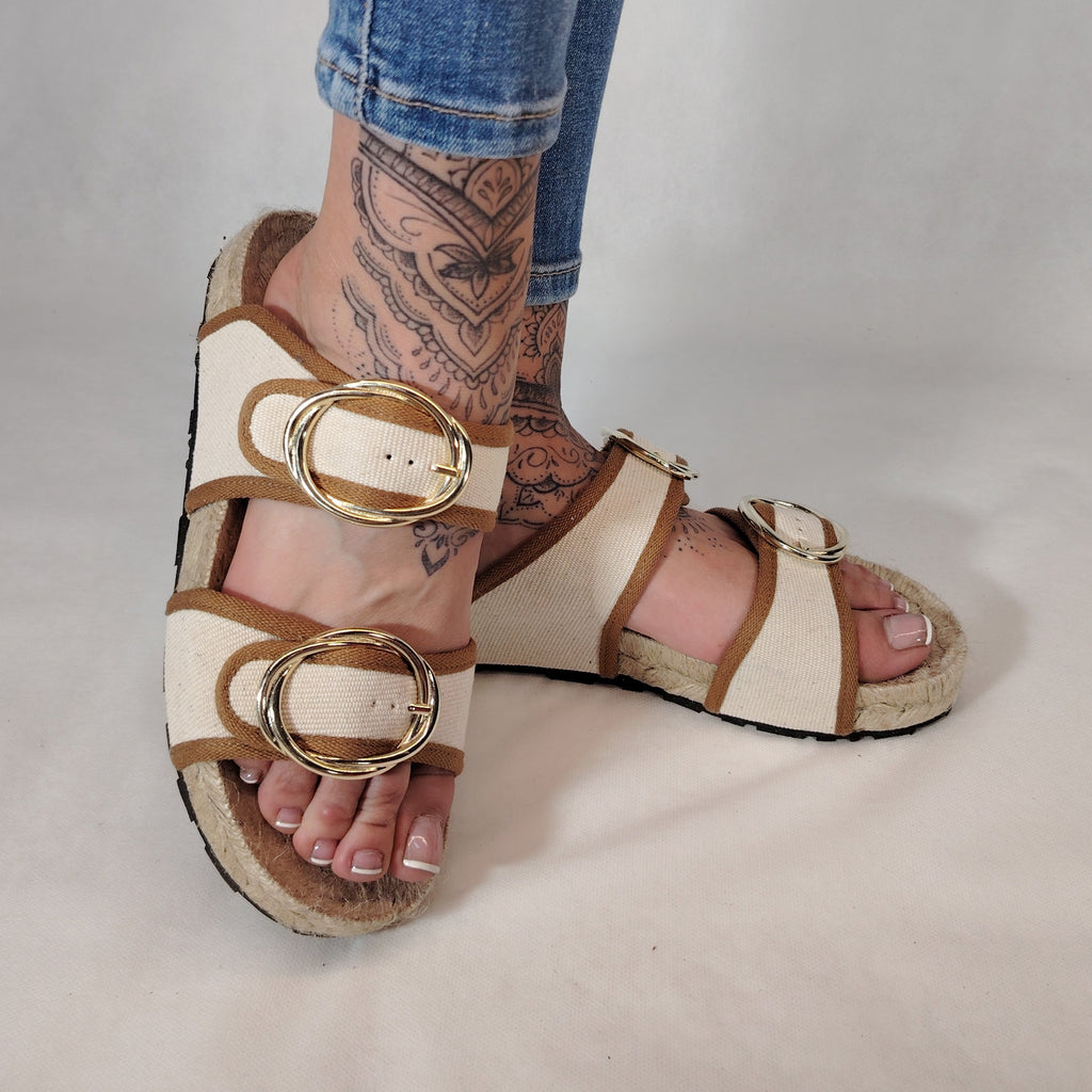 Sandalia plana de yute natural con corte en tejido color blanco y detalles en cuero con 2 hebillas y diseño artesanal de verano.