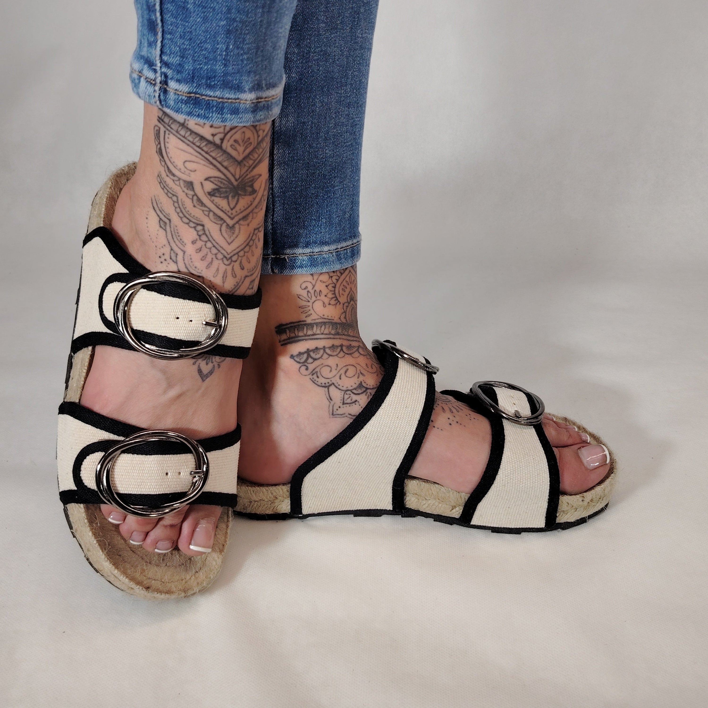 Sandalia plana de yute natural con corte en tejido color blanco y detalles en negro con 2 hebillas y diseño artesanal de verano.