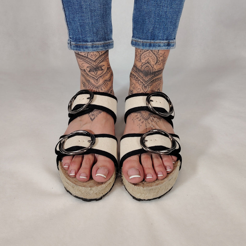 Sandalia plana de yute natural con corte en tejido color blanco y detalles en negro con 2 hebillas y diseño artesanal de verano.